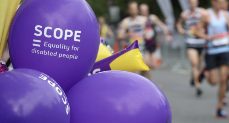 purple balloons that say Scope in the foreground while people run a race behind them