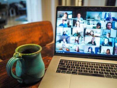 A blue mug sits by a macbook pro screen, which is filled with faces on a video call