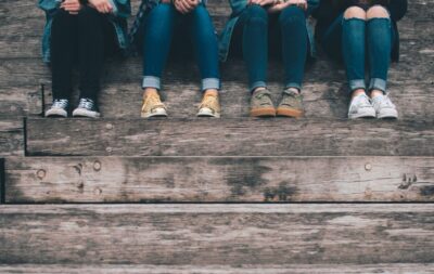 The legs of 4 teenagers clad in jeans, sitting on wooden steps
