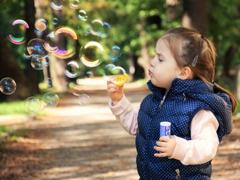 A young girl blows bubbles in a park