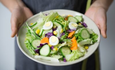 hands holding a plate full of a mixed salad including eggs lettuce cucumber and carrot