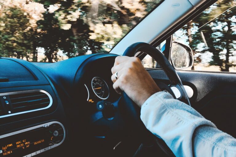 A woman's hand on the steering wheel with a blur of trees in the background
