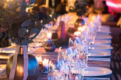 A long table set out for a grand dinner with wine glasses, white plates and candles
