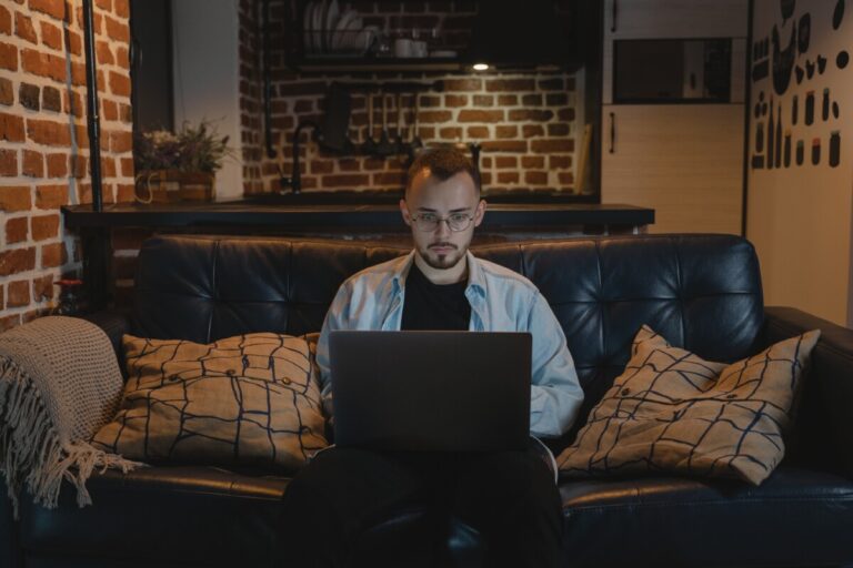 A man sits on his leather sofa looking at his laptop