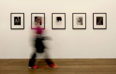 the blur of a person walks past a row of photos in the Tate
