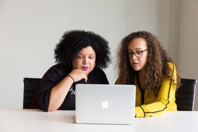 two women of colour look at a laptop screen
