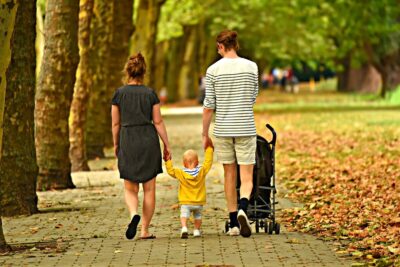 a family walking on a path in a park with trees on the left and leaves on the ground