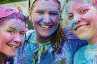 Three teenage girls covered in paint powder smile at the camera