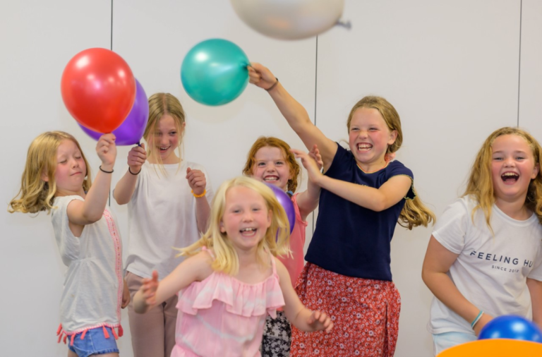 A group of young girls at a party laughing with balloons
