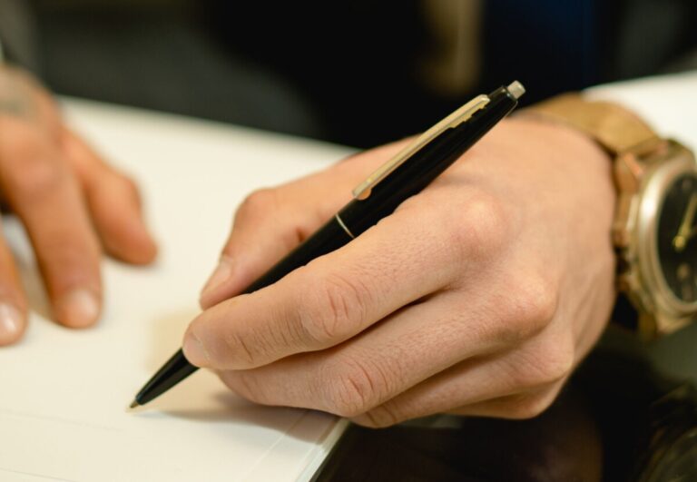 A hand holds a pen, about to write on a piece of paper