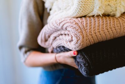 A woman carries a pile of jumpers. Photo by Dan Gold on Unsplash