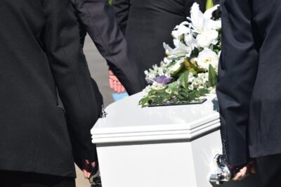 men dressed in black suits carry a white coffin.