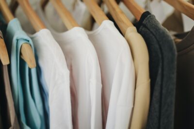 a row of tops and t-shirts on wooden hangers. Photo by Polina Tankilevitch