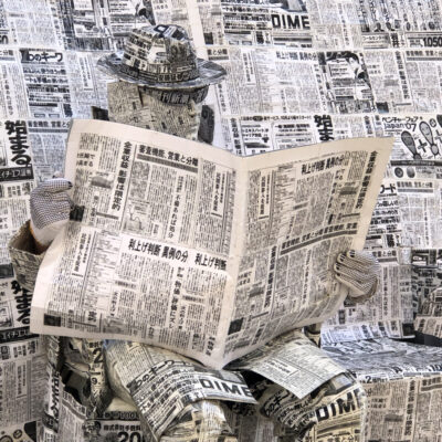 Street artist wrapped in newspaper reading a newspaper. Photo: Howard Lake