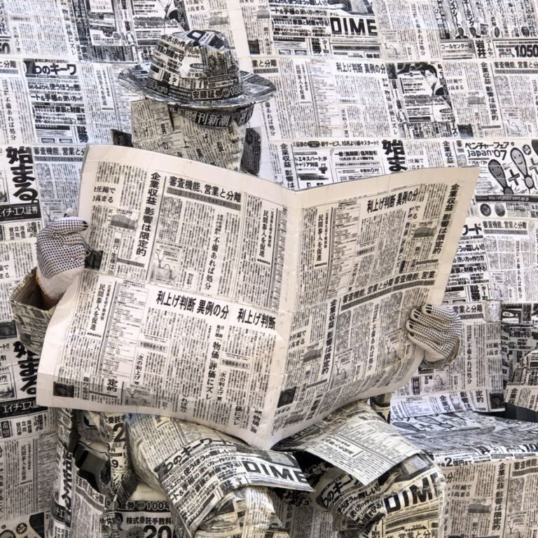 Street artist wrapped in newspaper reading a newspaper. Photo: Howard Lake