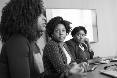 Three Black business women talk at an office desk. By Christina Morillo on Pexels