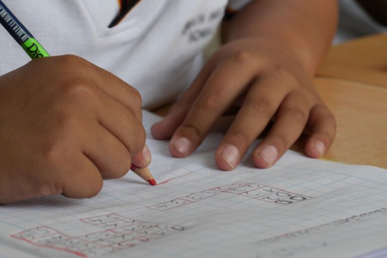 a child's hands hold a pencil as they do maths in an exercise book. Photo by Pixabay