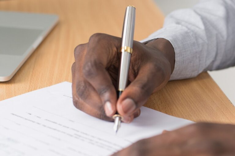 A man's hand holds a pen and signs a document. By Cytonn Photography on Pexels