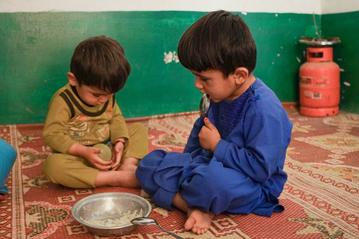 Aina*’s children, Amin* and Abas*, sit on a plastic mat with a bowl of rice at their home in their village in Daykundi Province, Afghanistan on 28 May 2022. DEC member CAFOD has worked with their partner Caritas Germany to provide cash distributions for families to buy food in Afghanistan, where 95% of people do not have enough to eat.