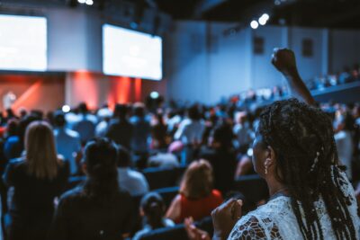 A woman raises her hand in a conference. By Luis Quintero on Pexels