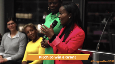 An image from Money4YOU's Dragon's Den showing a woman in a red suit addressing an audience