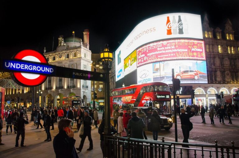 Piccadilly Circus at night showing the tube station entrance and illuminated billboards. Image by Rudy and Peter Skitterians from Pixabay