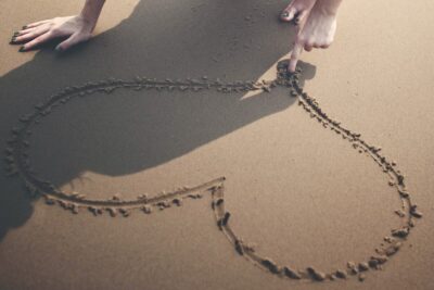A woman draws a heart in the sand. Photo by Pixabay
