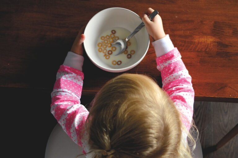 An over the head shot looking down at a small child in a pink top eating a bowl of cereal. By Stocksnap on Pixabay