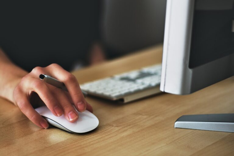 A woman's hand on a computer mouse, also holding a pen. By Vojtech Okenka on Pexels