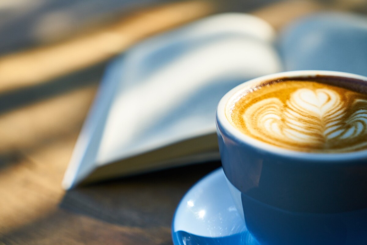 A coffee in a blue cup in front of an open book. By Engin Akyurt on Pixabay