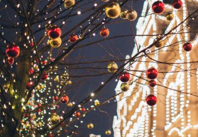 Christmas baubles on a tree outside a building covered in white Christmas lights. By Elina Fairytale on Pexels
