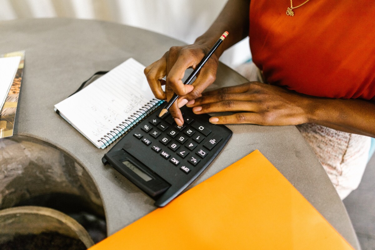 A woman inputs figures into a calculator, with a notepad by her side. By Rodnae Productions on Pexels