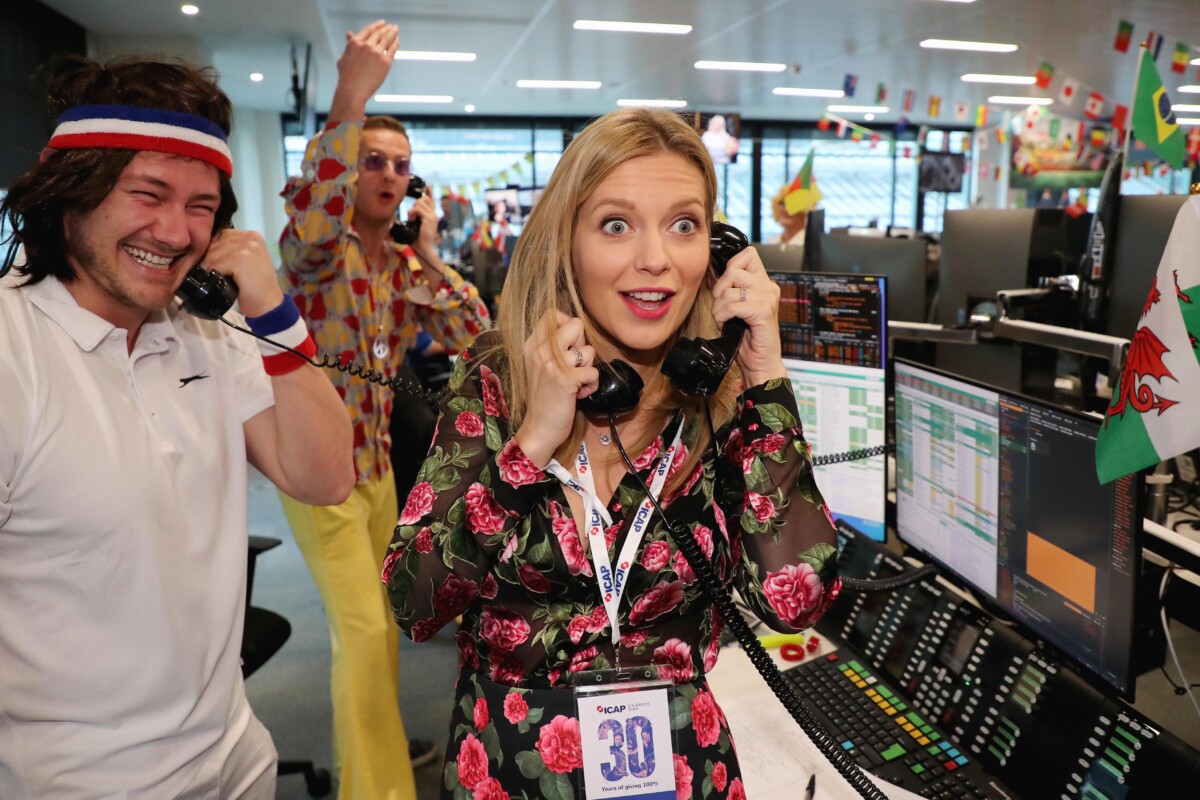 Rachel Riley at ICAP Charity Day, holding two phones, besides ICAP staff in fancy dress.