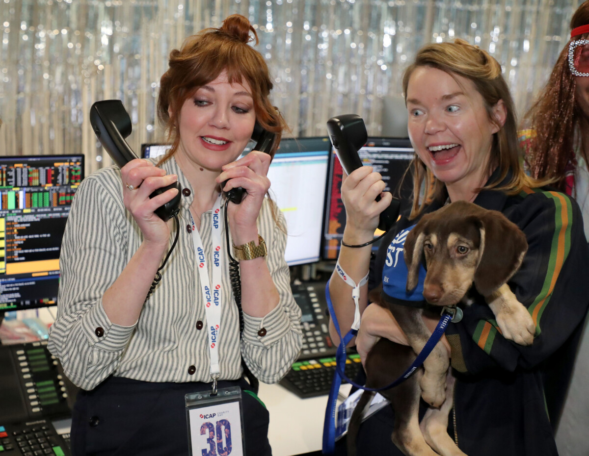 Anna Maxwell Martin (r) and Diane Morgan at ICAP Charity Day 2022. Both are holding phones, and Maxwell Martin is holding a small dog with a Battersea coat.