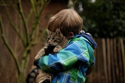 A boy in a blue & green check jacket hugs a tabby cat. By Westfale on pixabay