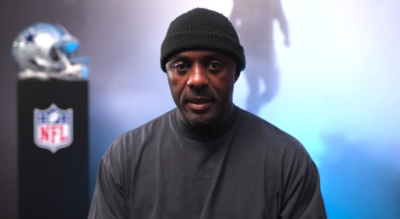 Idris Elba in black beanie, in front of an NFU stand