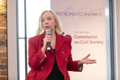 Deborah Meaden in a red jacket, speaks into a microphone as she addresses the audience at the launch of the Law Family Commission on Civil Society's final report launch