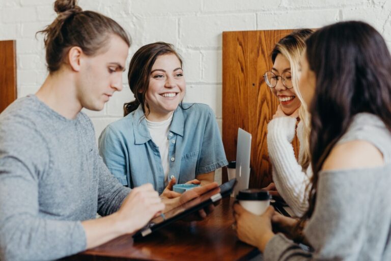 4 young people huddle over a table, launching. By Brooke Cagle on Unsplash