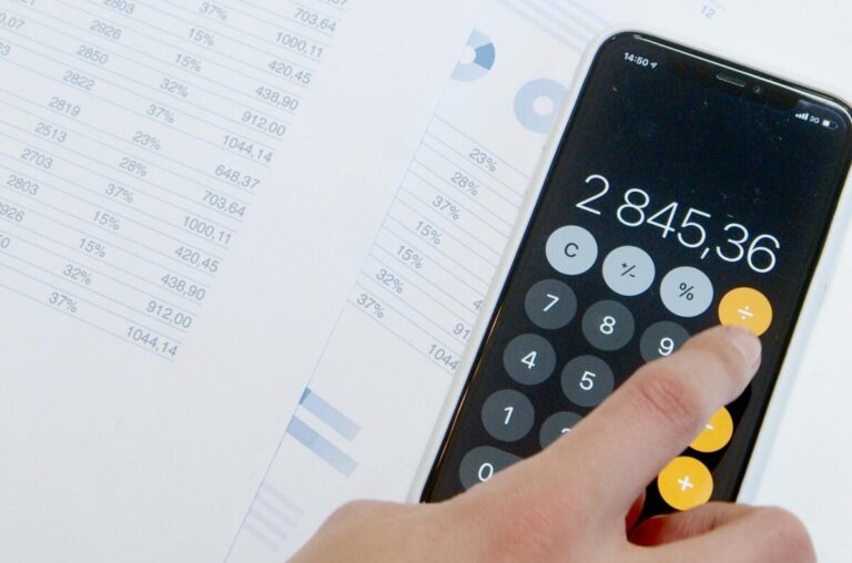 A hand on an iphone calculator, on top of sheets of business figures. By Artem Podrez on Pexels