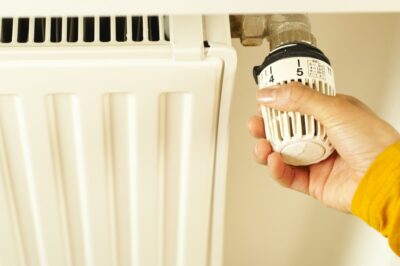 A hand turns down the dial on a radiator. By Boom on Pexels