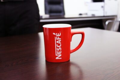Red Nescafe mug on a table. Photo by Nkmgroup Nkm: https://www.pexels.com/photo/red-and-white-nescafe-printed-mug-on-brown-wooden-table-1002649/