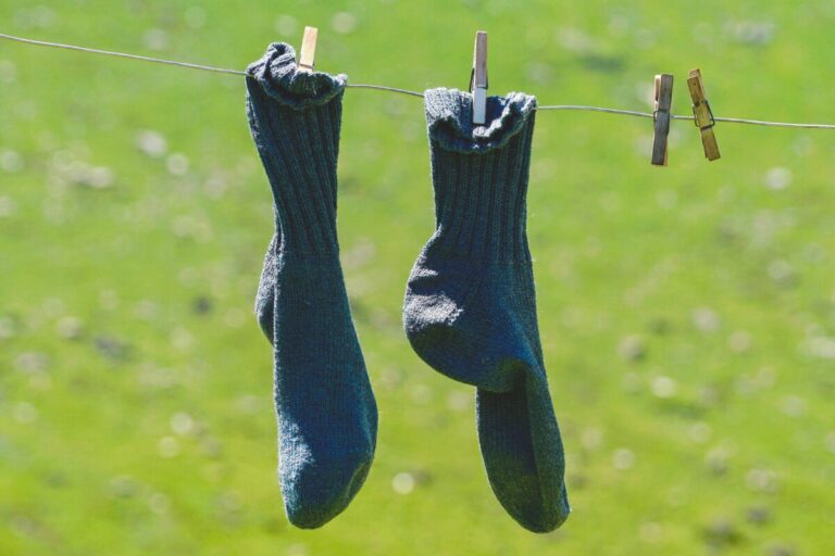 Pair of socks hanging on a washing line, against a background of grass. Two clothes pegs are next to them.