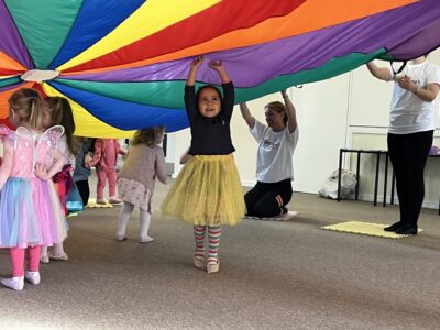 Toddlers dance under a rainbow parachute at a babyballet danceathon