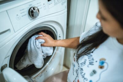 A woman puts clothing in a washing machine. By Rodnae Productions on pexels