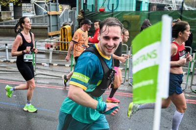 A runner in the London Marathon wearing a Samaritans top, runs past a Samaritans flag.
