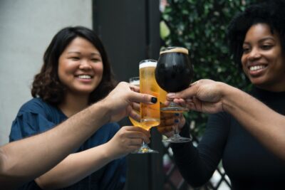 Women smile as they clink glasses of beer. By Elevate on Pexels