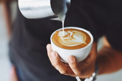 A barista pours the milk into a coffee, creating a flower pattern on the surface. By Chevanon Photography on Pexels