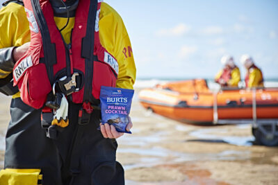 An RNLI lifeboat volunteer holds a packet of fundraising Burts chips