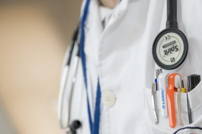 close up of a doctor's white coat, stethoscope and pens in their pocket. By Darkostojanovic