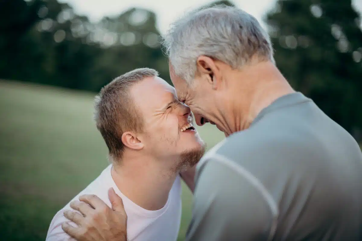 A young man with Downs and his father embrace, laughing. By Nathan Anderson on Unsplash.